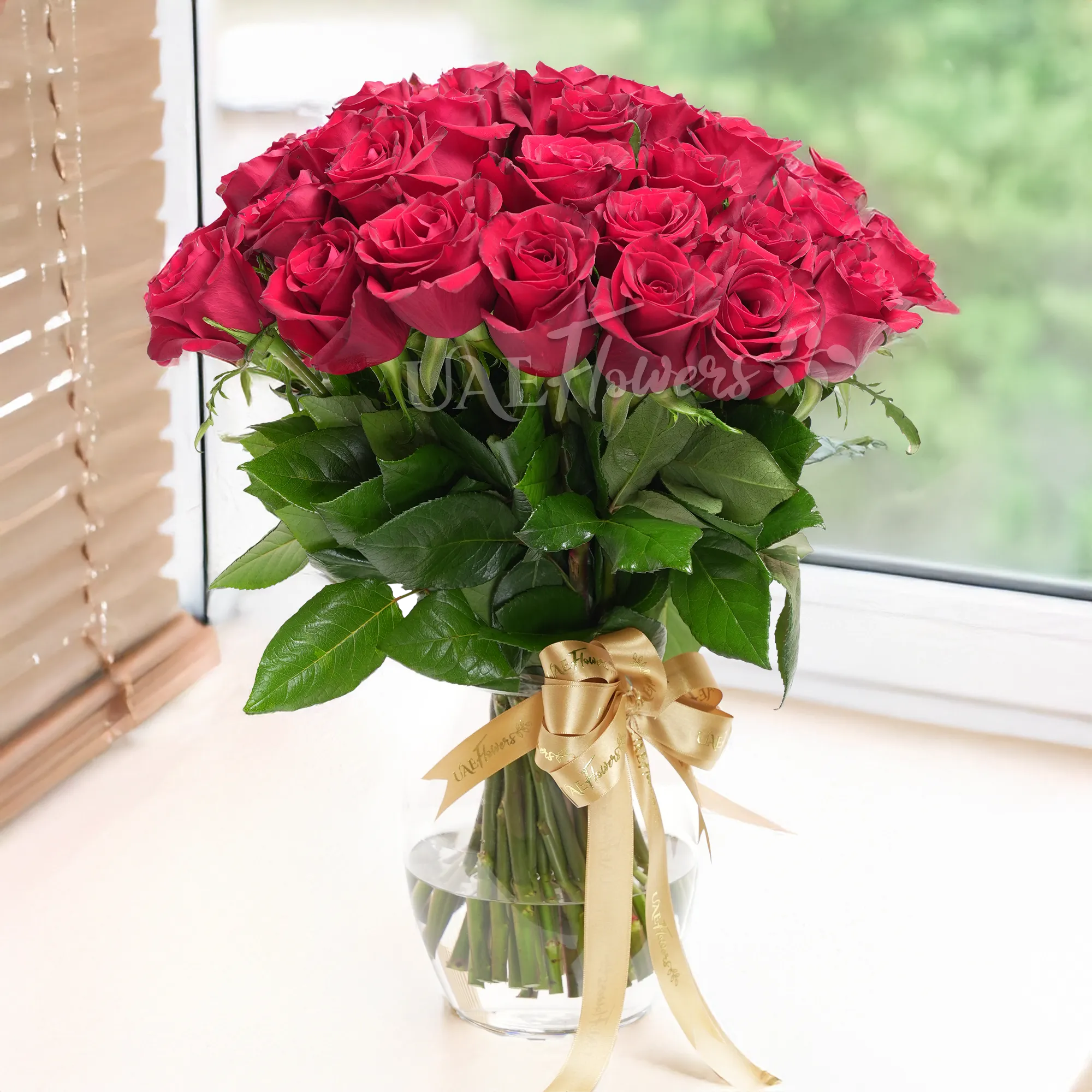 A vase arrangement of 50 red roses with green fillers and tied with golden ribbons.