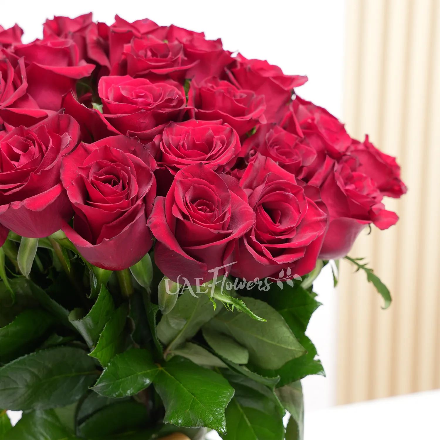 A vase arrangement of 50 red roses with green fillers and tied with golden ribbons.