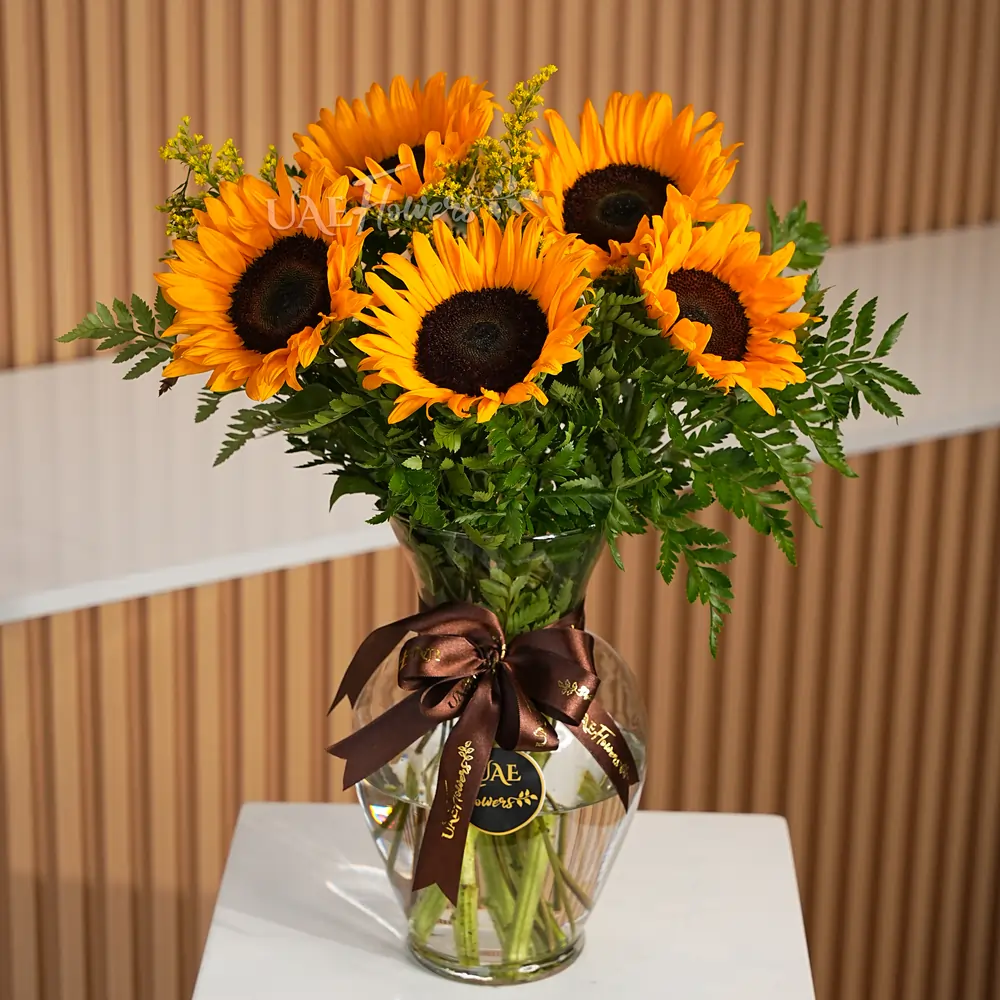 5 stems of sunflowers with fillers in a glass vase.