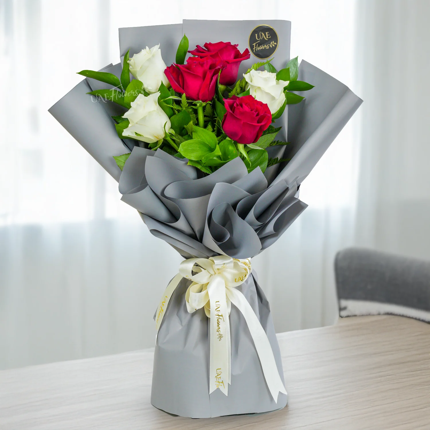 Bouquet of 6 red & white roses with green fillers in paper packing tied with ribbons.