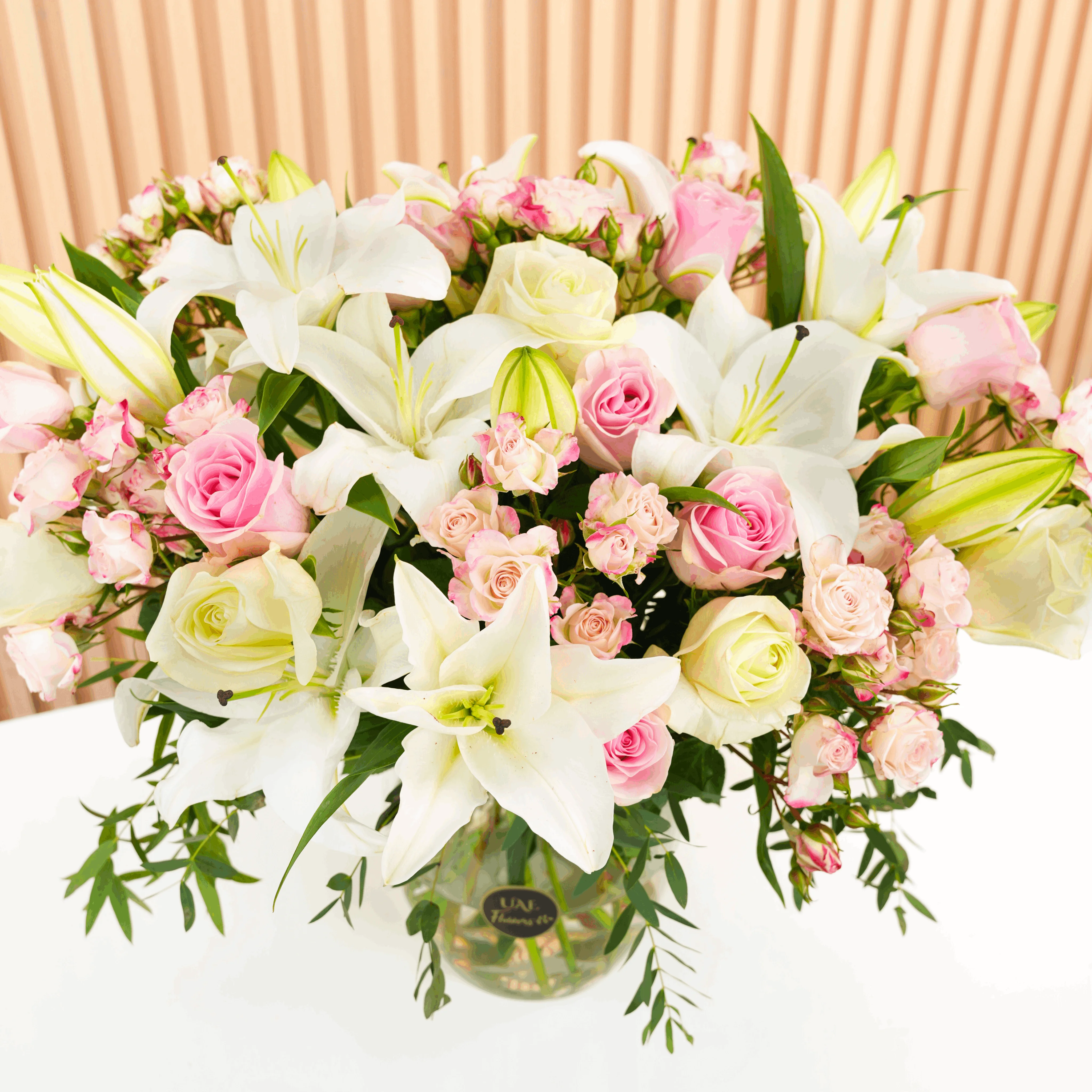 white lilies, white roses, pink roses, pink spray roses with green fillers in a glass vase.