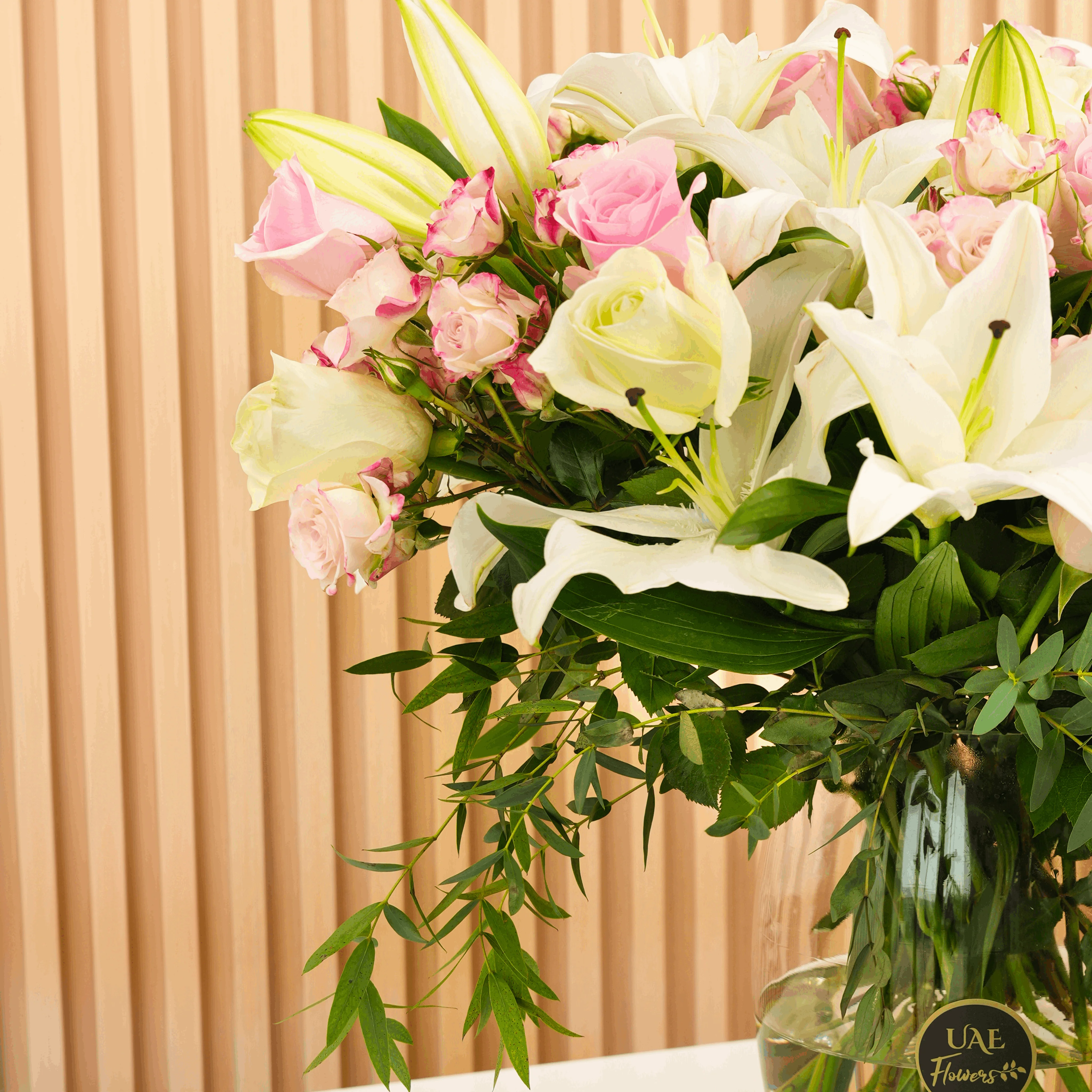 white lilies, white roses, pink roses, pink spray roses with green fillers in a glass vase.