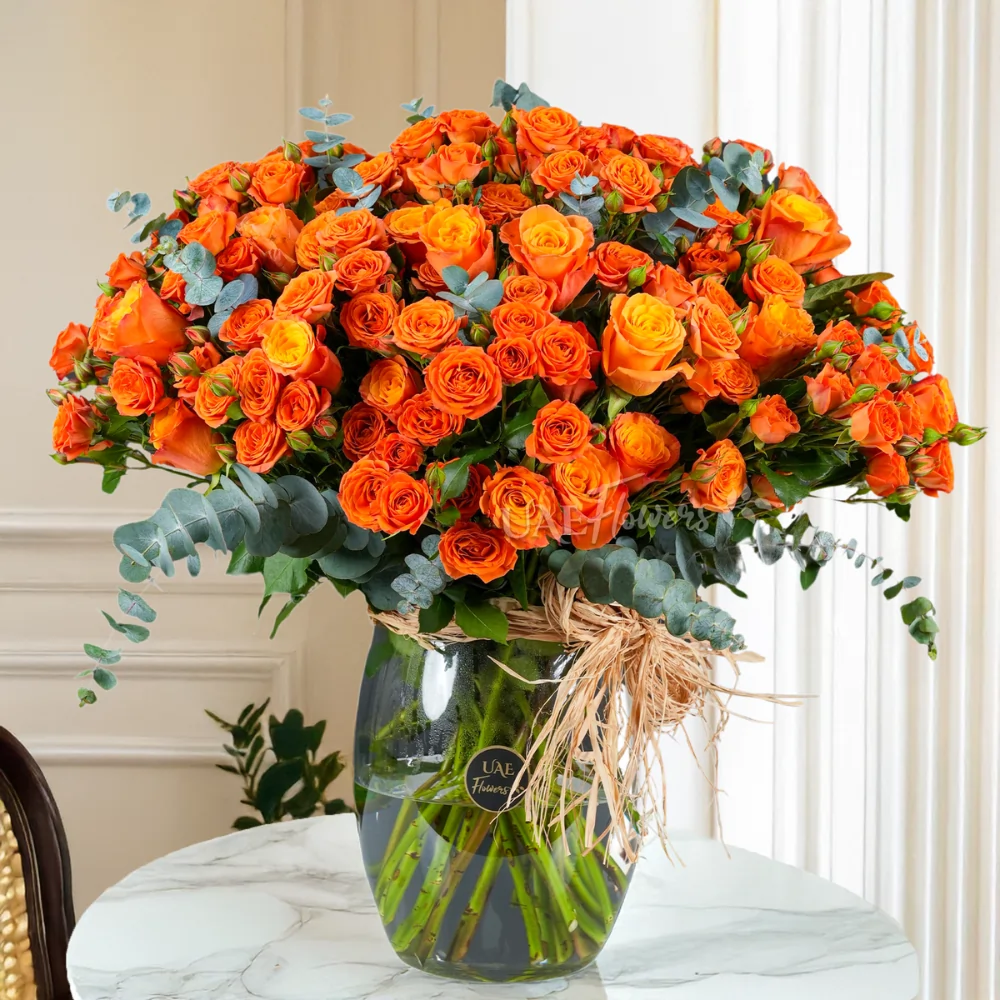 A glass vase of 20 spray roses and 20 orange roses in a glass vase with green fillers.