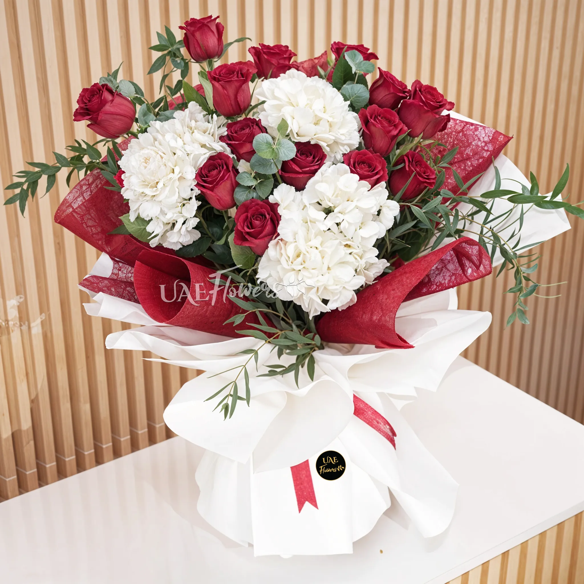 Bouquet of 3 white hydrangeas, 15 red roses with eucalyptus leaf fillers wrapped in red and white wrapping paper tied with red color ribbons.