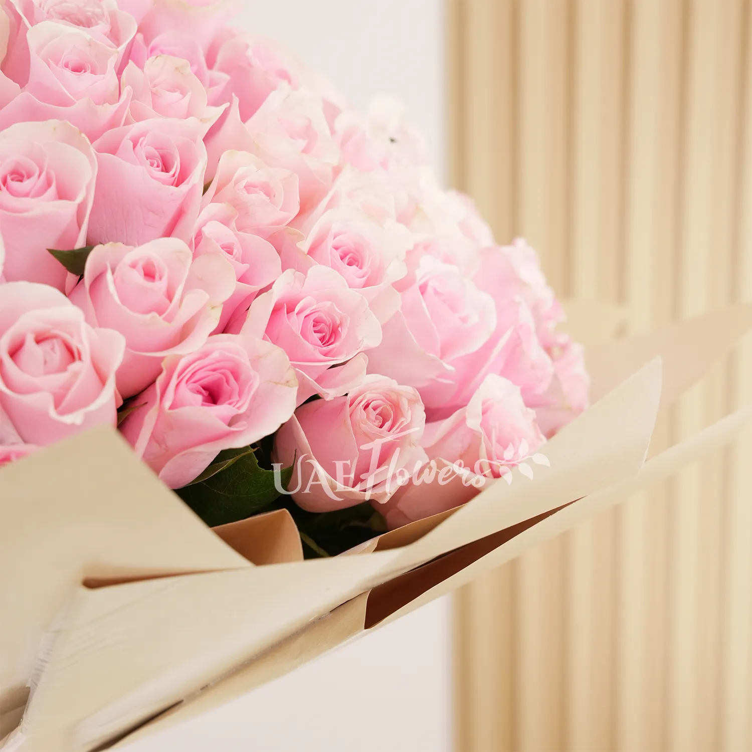 Bouquet of 200 pink roses with fillers in brown paper packing tied with pink ribbons.