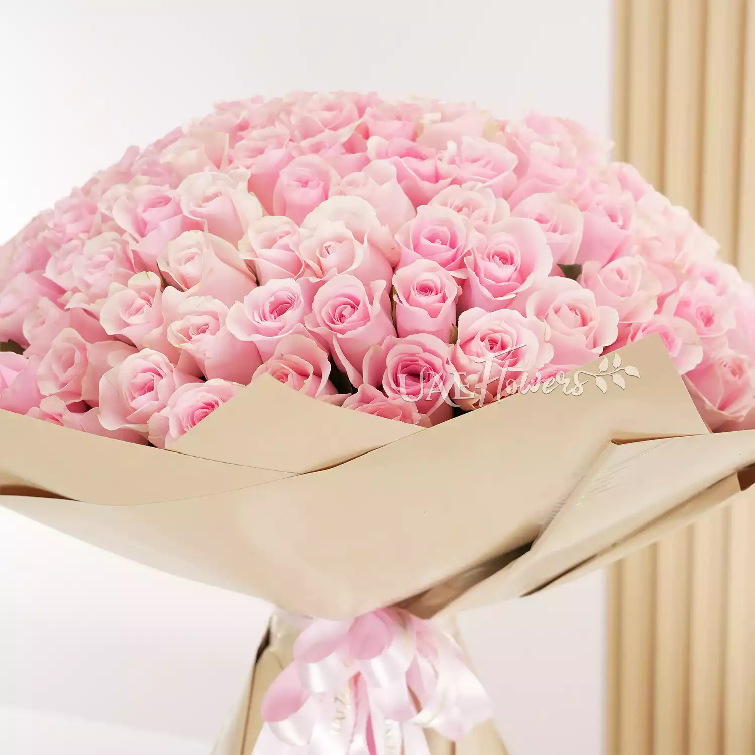 Bouquet of 200 pink roses with fillers in brown paper packing tied with pink ribbons.