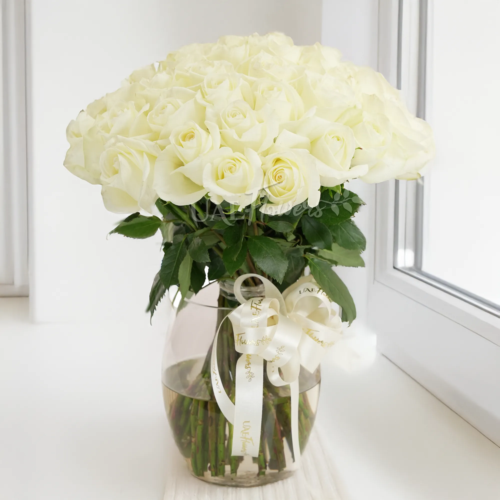 A vase arrangement of 40 white roses with green fillers tied with white ribbons.
