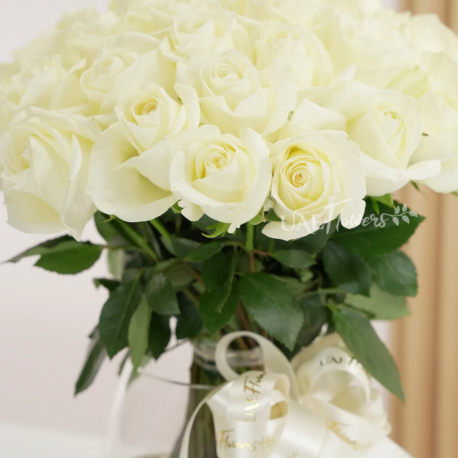 A vase arrangement of 40 white roses with green fillers tied with white ribbons.