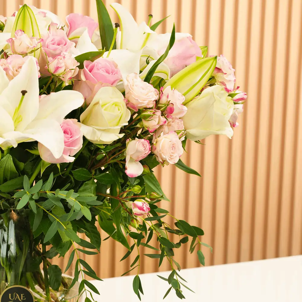 white lilies, white roses, pink roses, pink spray roses with green fillers in a glass vase.