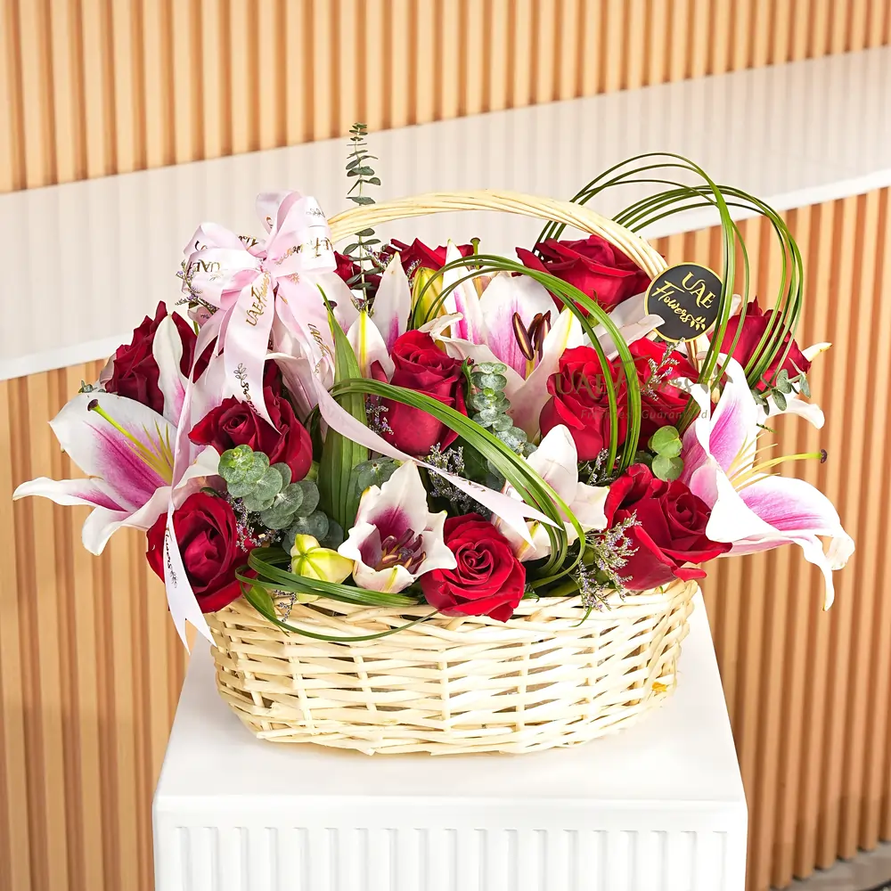 Arrangement of 12 red roses and 3 pink lilies with eucalyptus leaf & green fillers with a touch of steel grass in a basket.