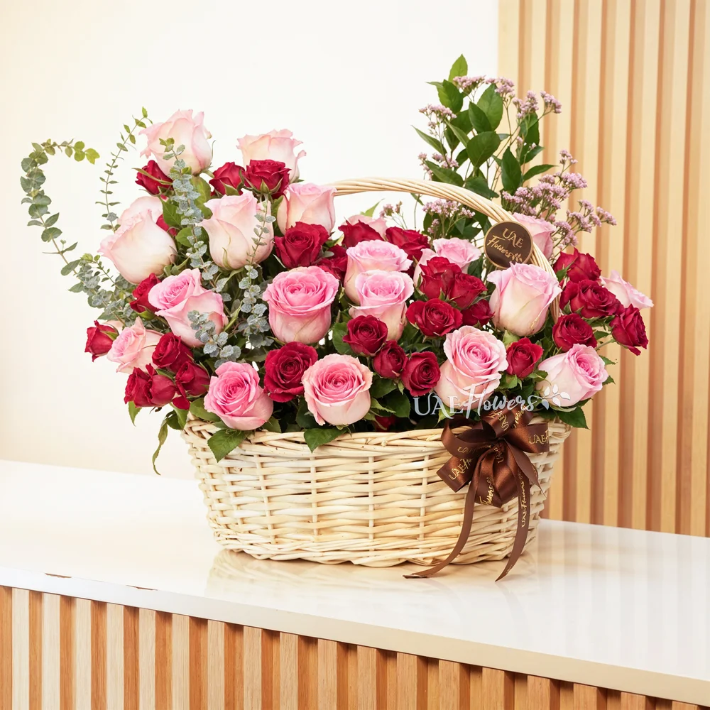 An arrangement of 20 pink roses and 6 red spray roses with eucalyptus leaf and green fillers in a handle basket.