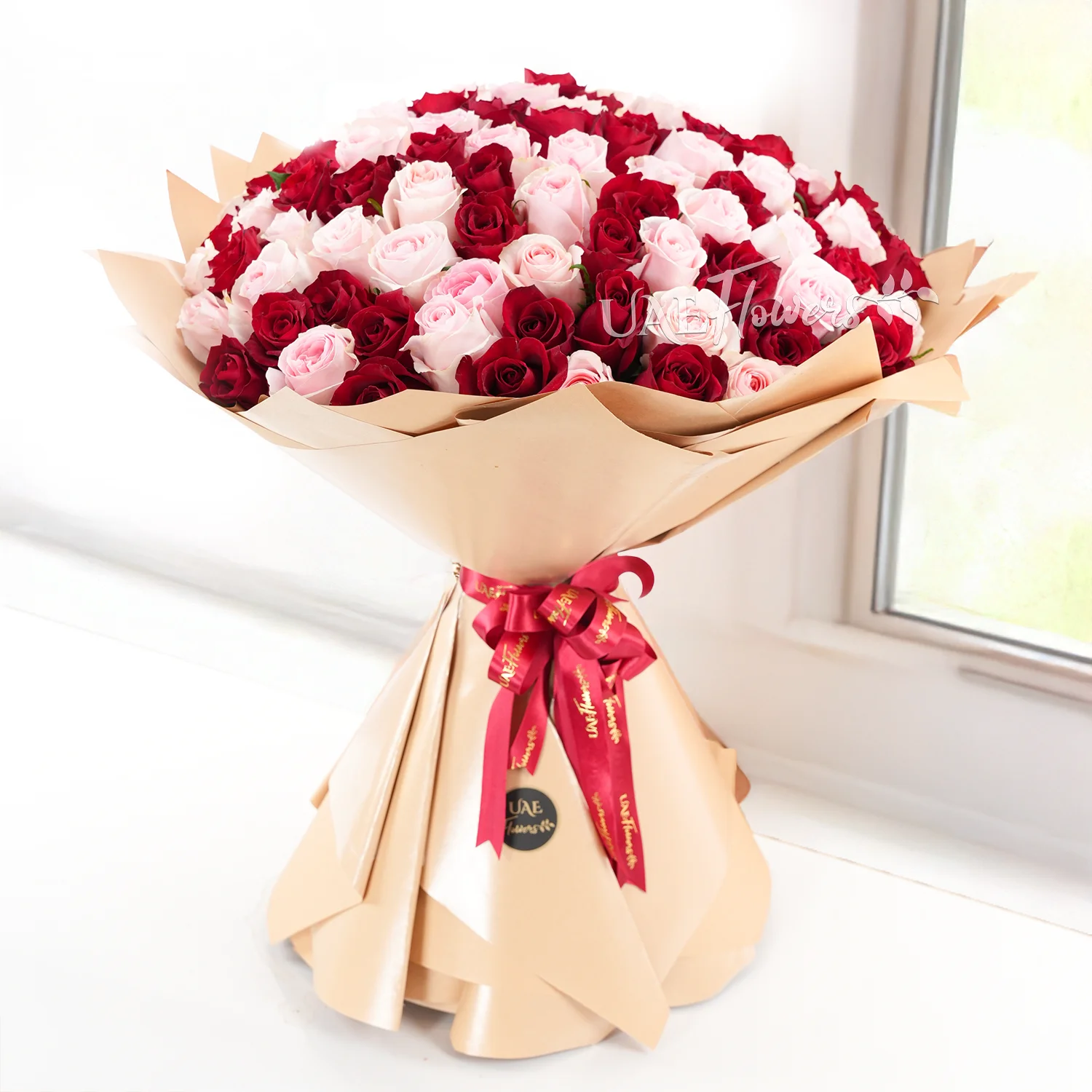 Bouquet of 100 red and pink roses with fillers in brown wrapping paper and tied with ribbons.