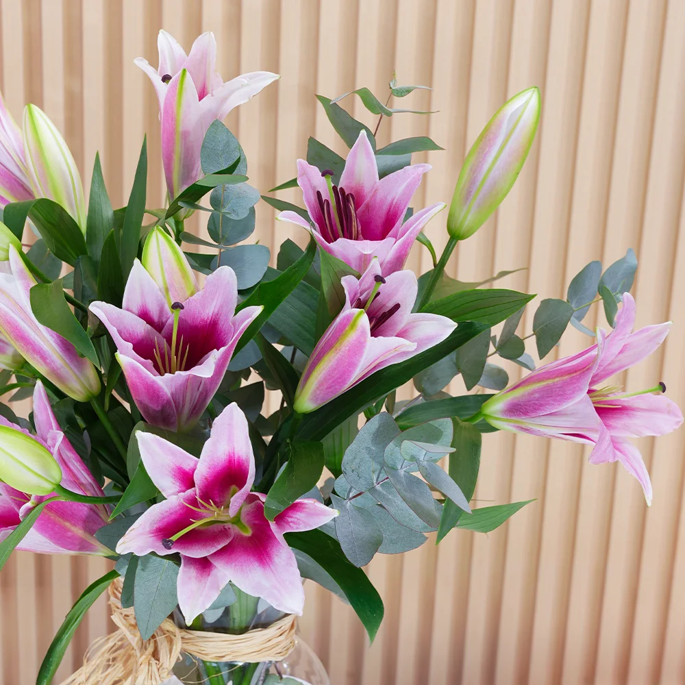 5 pink lilies with green fillers in a glass vase