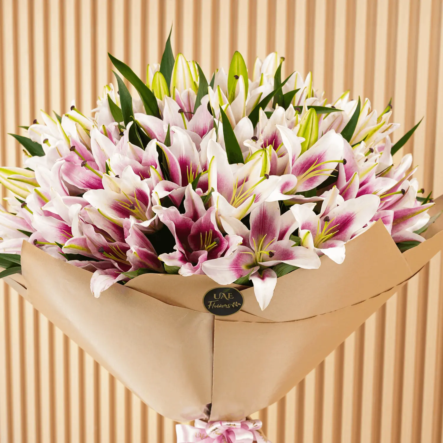 Bouquet of 20 pink lilies with fillers in brown wrapping paper and tied with ribbons.
