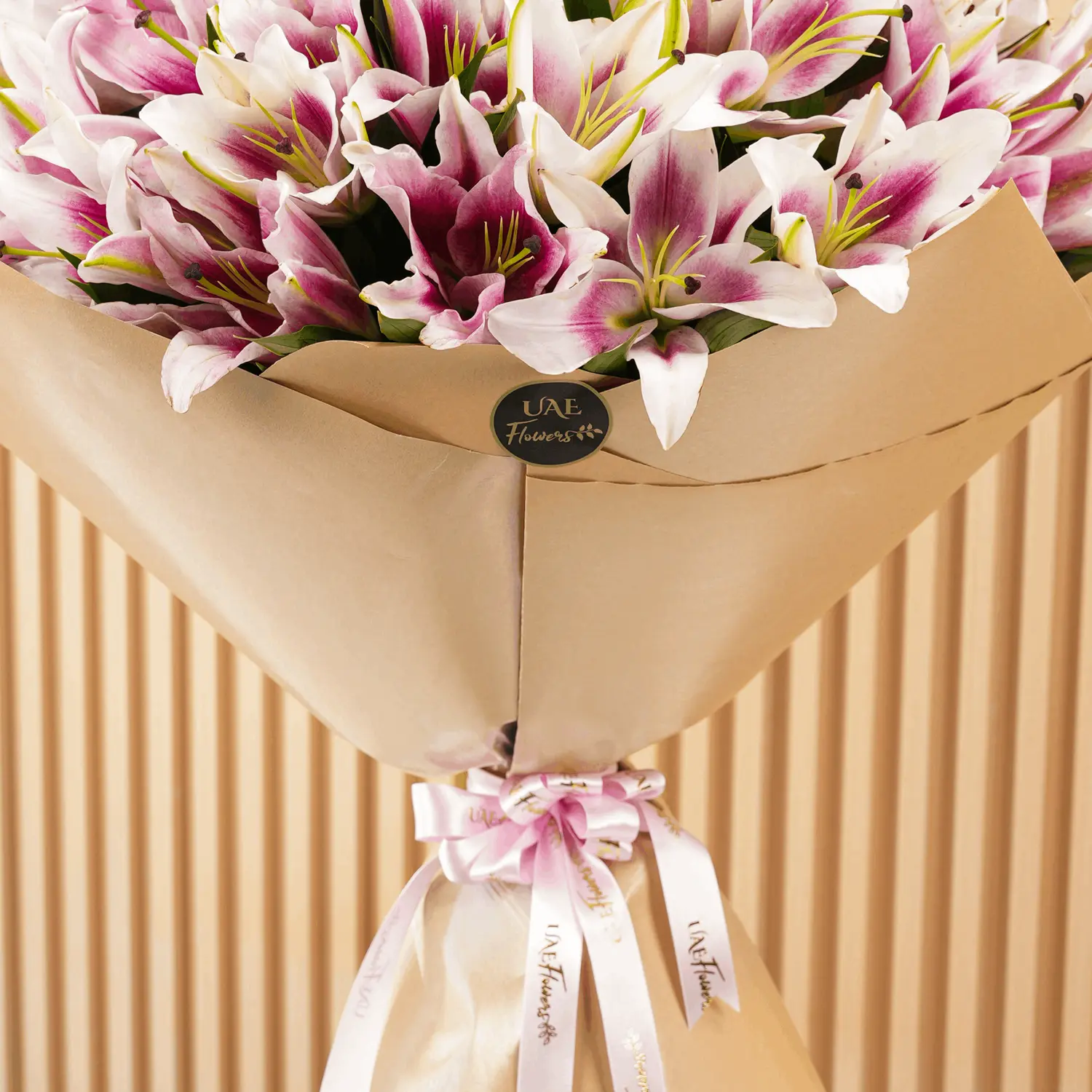 Bouquet of 20 pink lilies with fillers in brown wrapping paper and tied with ribbons.