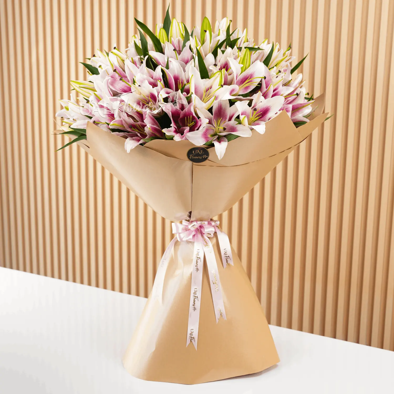 Bouquet of 20 pink lilies with fillers in brown wrapping paper and tied with ribbons.