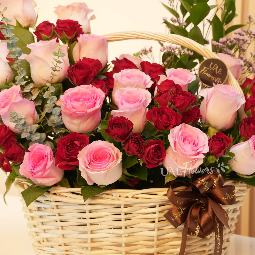 An arrangement of 20 pink roses and 6 red spray roses with eucalyptus leaf and green fillers in a handle basket.