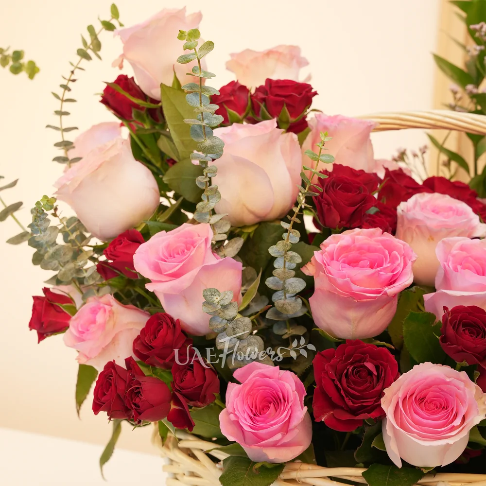 An arrangement of 20 pink roses and 6 red spray roses with eucalyptus leaf and green fillers in a handle basket.
