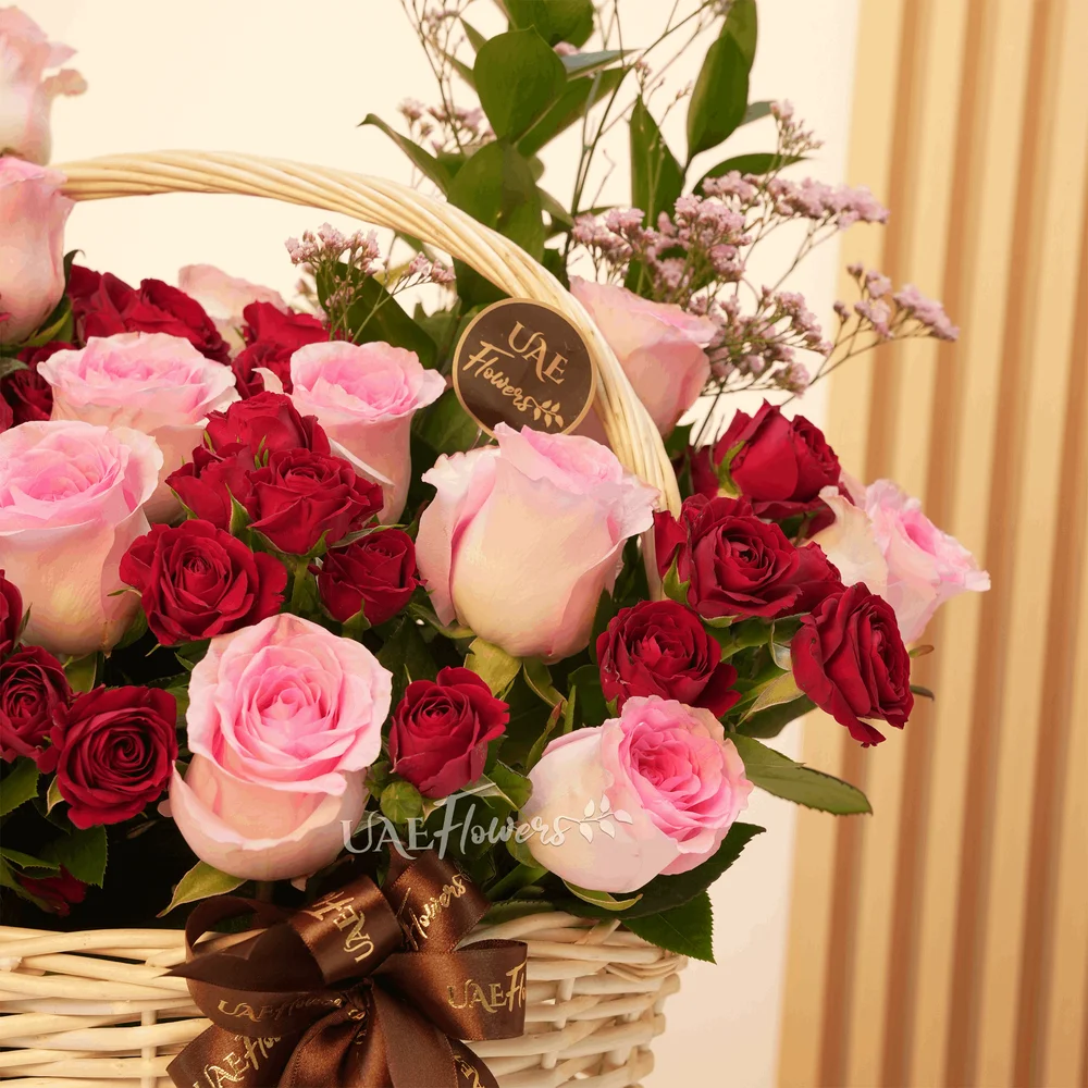 An arrangement of 20 pink roses and 6 red spray roses with eucalyptus leaf and green fillers in a handle basket.