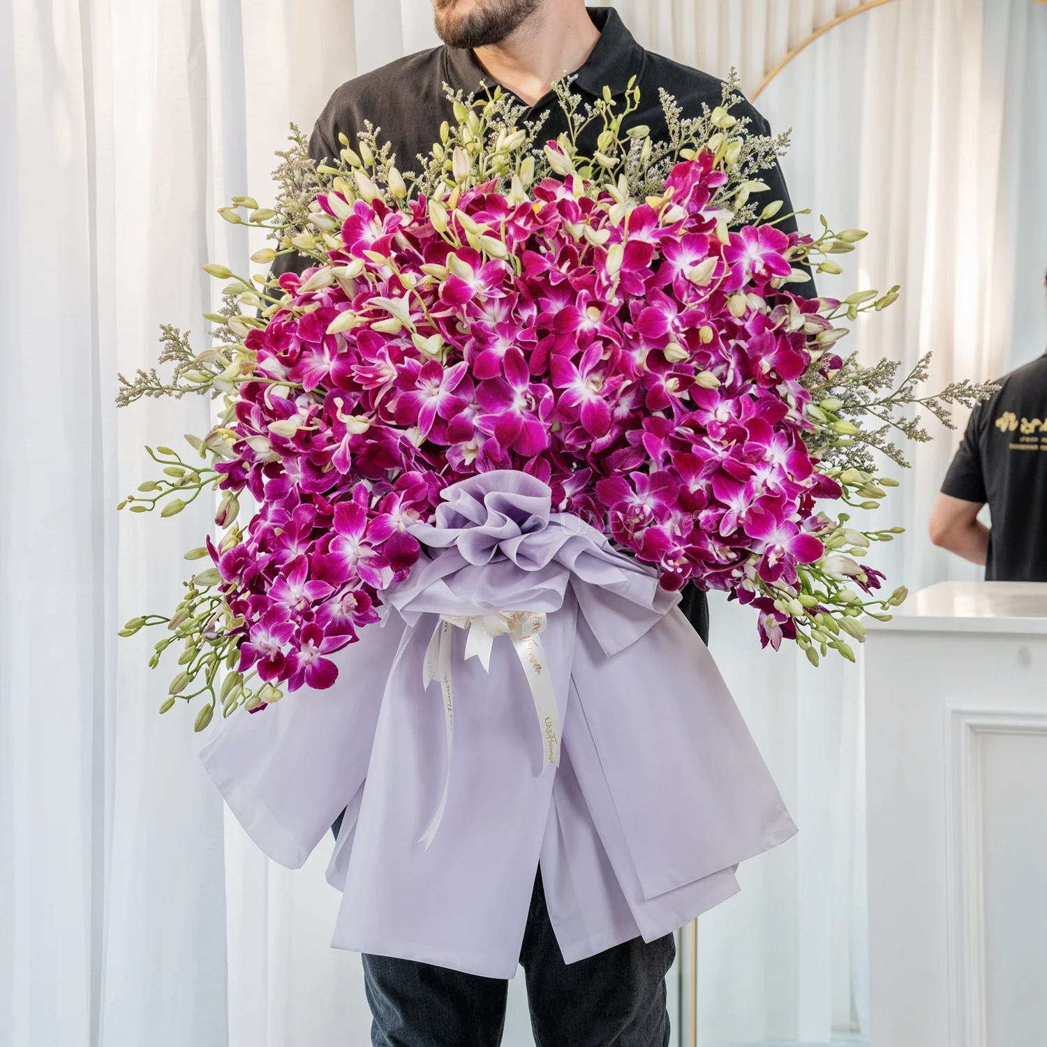 Bouquet of 80 purple orchids in paper packing tied with ribbons.