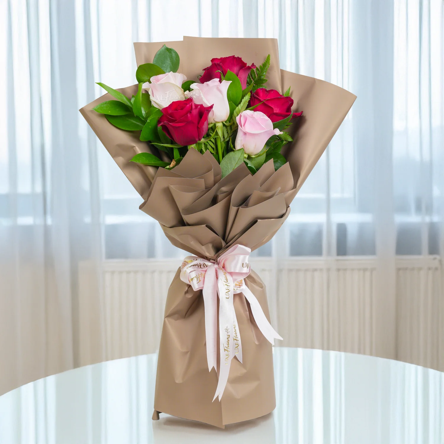 Bouquet of 6 red & pink roses with green fillers in paper packing tied with ribbons.