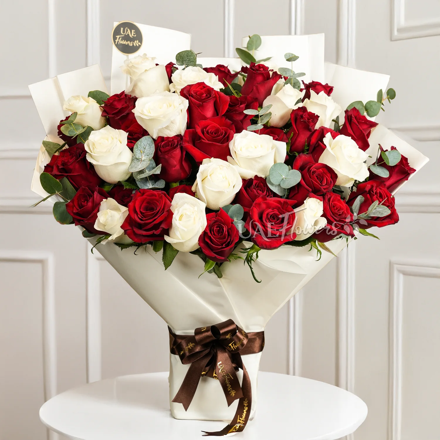 Bouquet of 25 red roses and 15 white roses with green fillers in paper packing tied with ribbons.