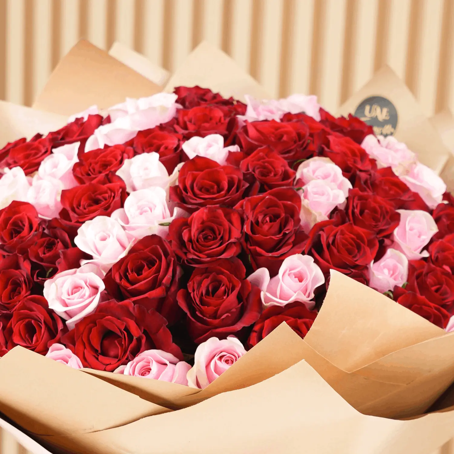 Bouquet of 100 red and pink roses with fillers in brown wrapping paper and tied with ribbons.
