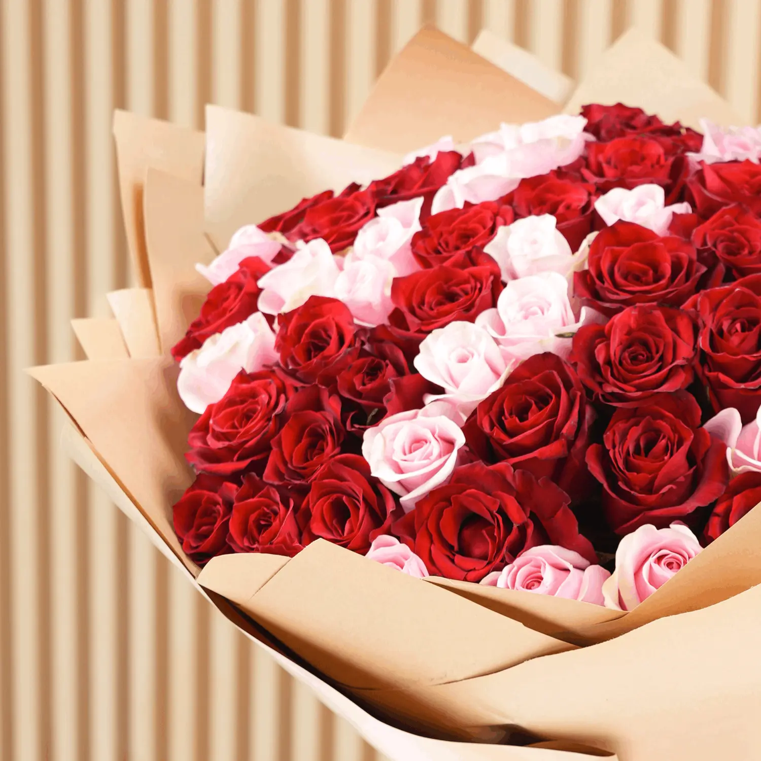 Bouquet of 100 red and pink roses with fillers in brown wrapping paper and tied with ribbons.