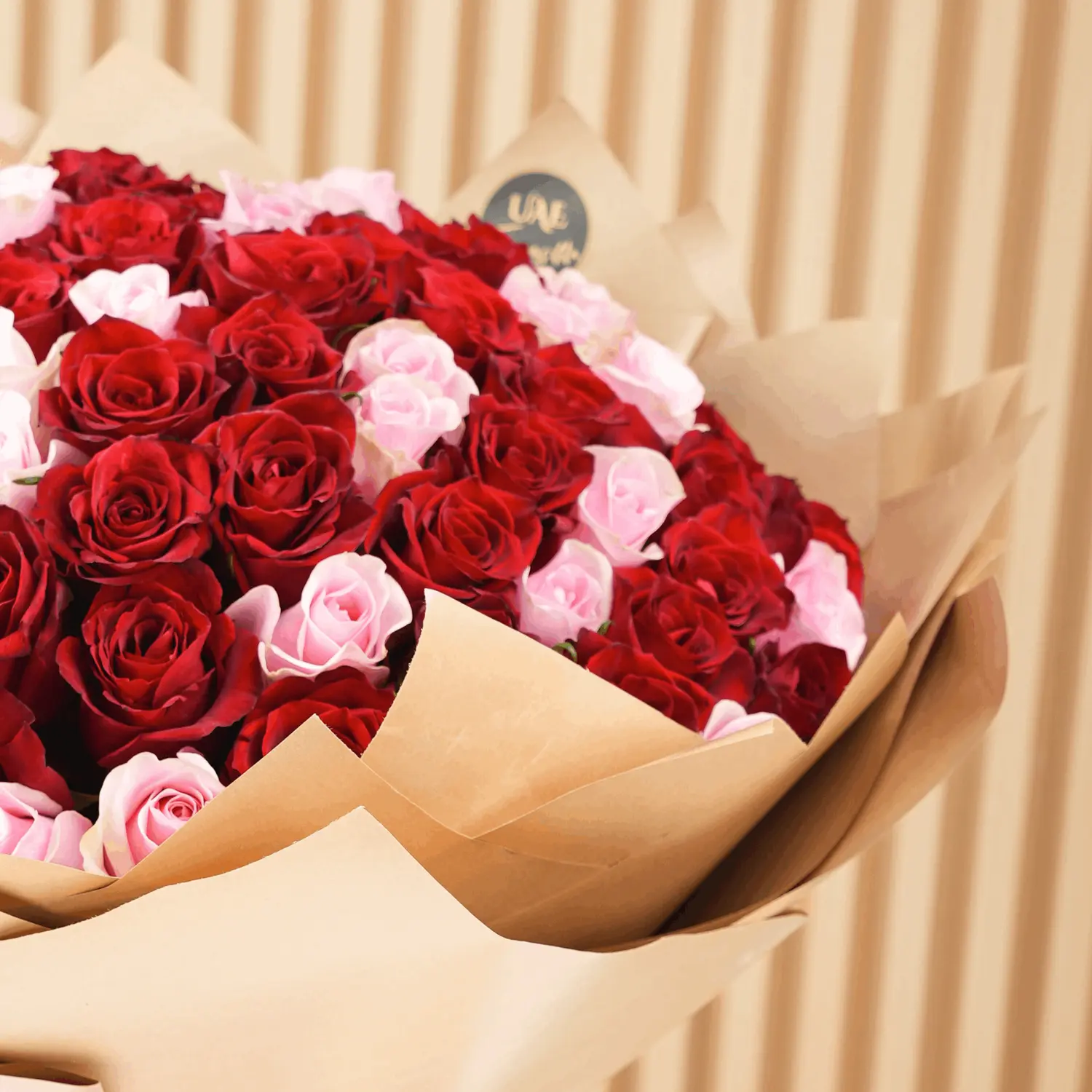 Bouquet of 100 red and pink roses with fillers in brown wrapping paper and tied with ribbons.