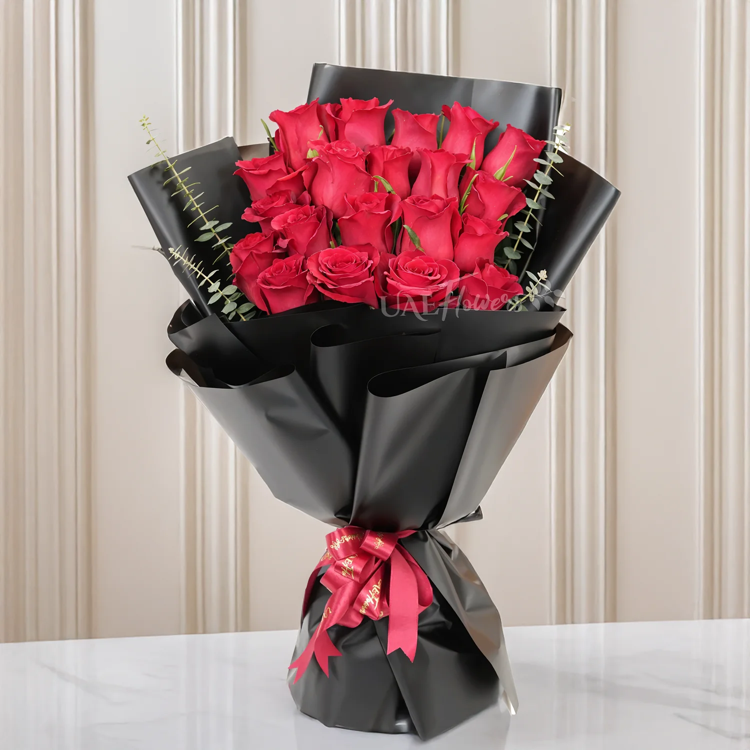 Bouquet of 20 red roses with green and eucalyptus leaf in black paper packing and tied with red ribbons.