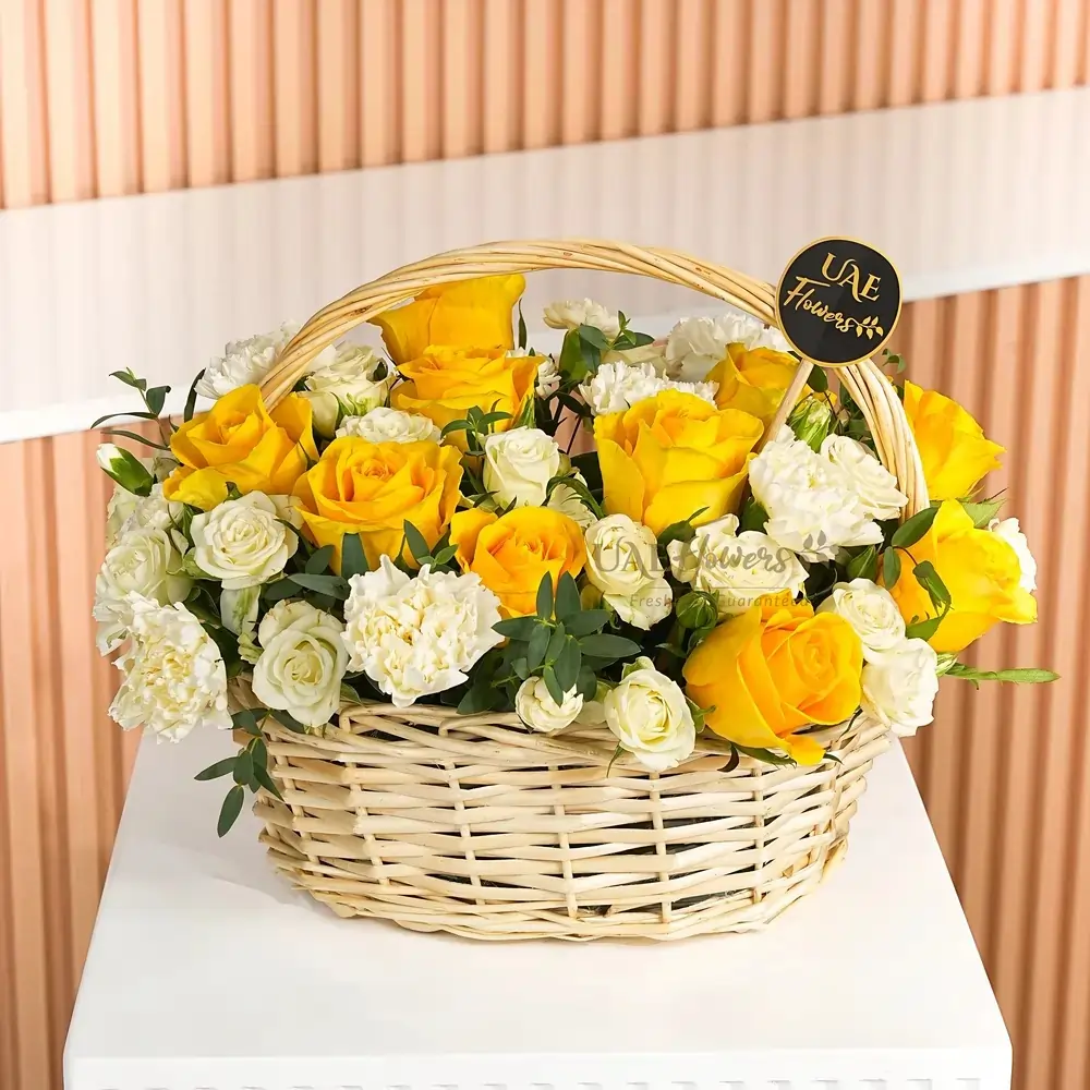 Arrangement of 10 yellow roses, 8 white carnations, 2 white spray roses with green fillers in a basket.