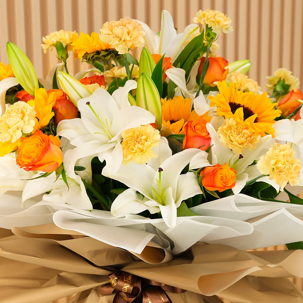 Bouquet of 5 white lilies, 5 sunflowers, 10 orange roses and 15 peach carnations with green fillers wrapped in paper packing and tied with ribbons.