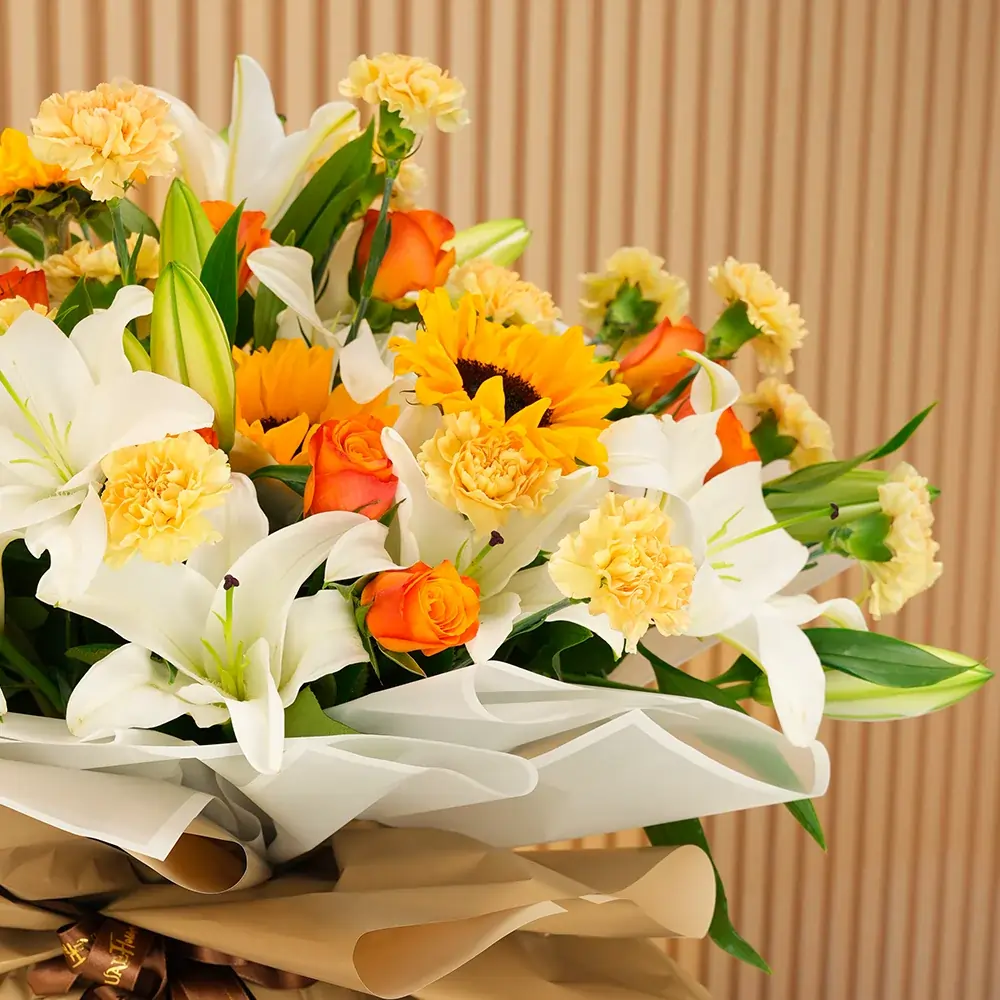 Bouquet of 5 white lilies, 5 sunflowers, 10 orange roses and 15 peach carnations with green fillers wrapped in paper packing and tied with ribbons.