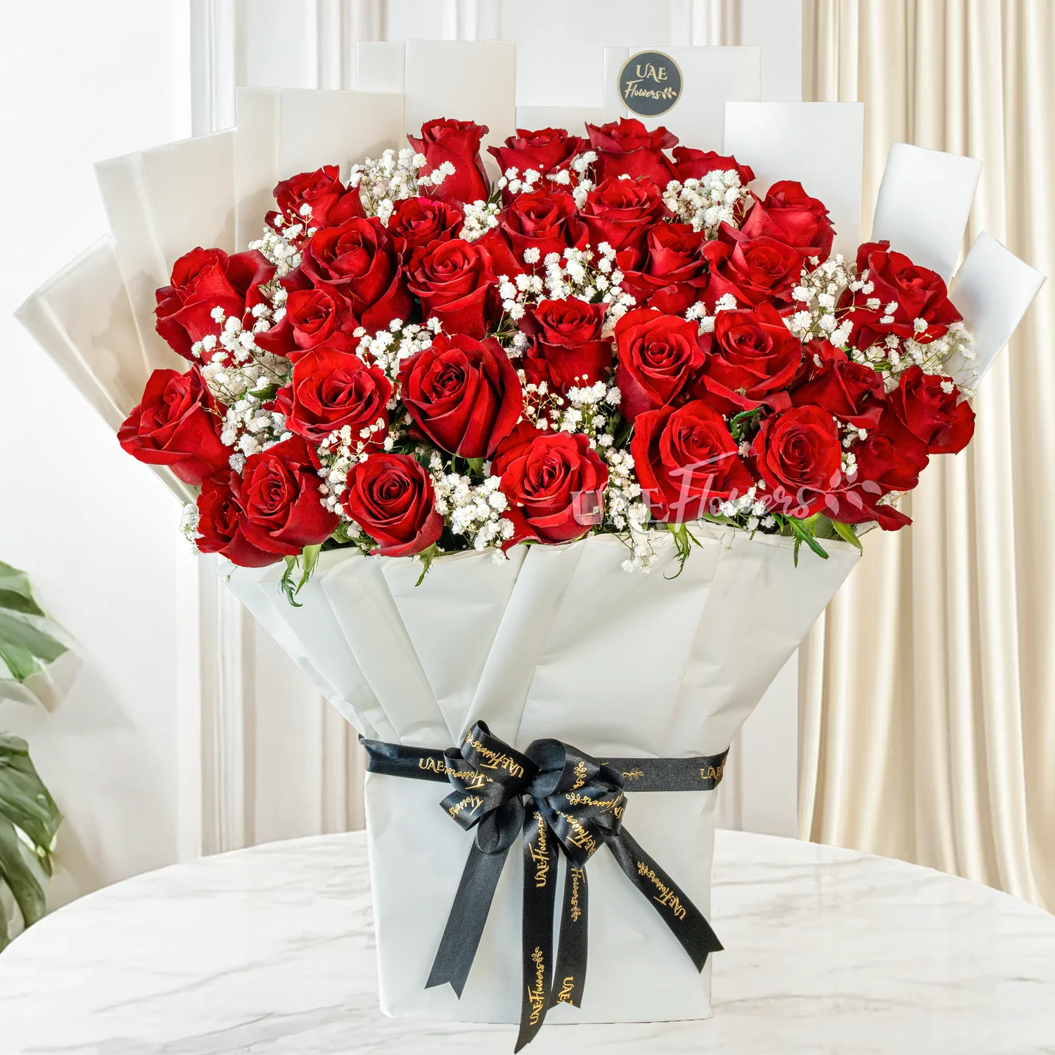 Bouquet of 30 red roses with green fillers in paper packing tied with ribbons.