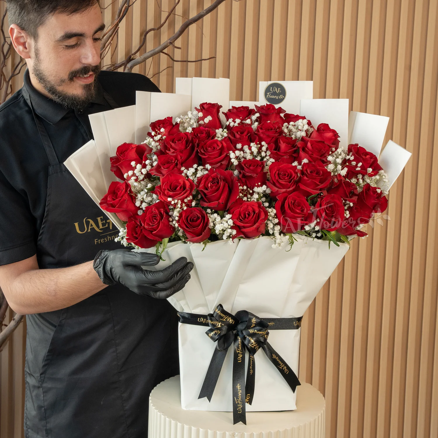 Bouquet of 30 red roses with green fillers in paper packing tied with ribbons.