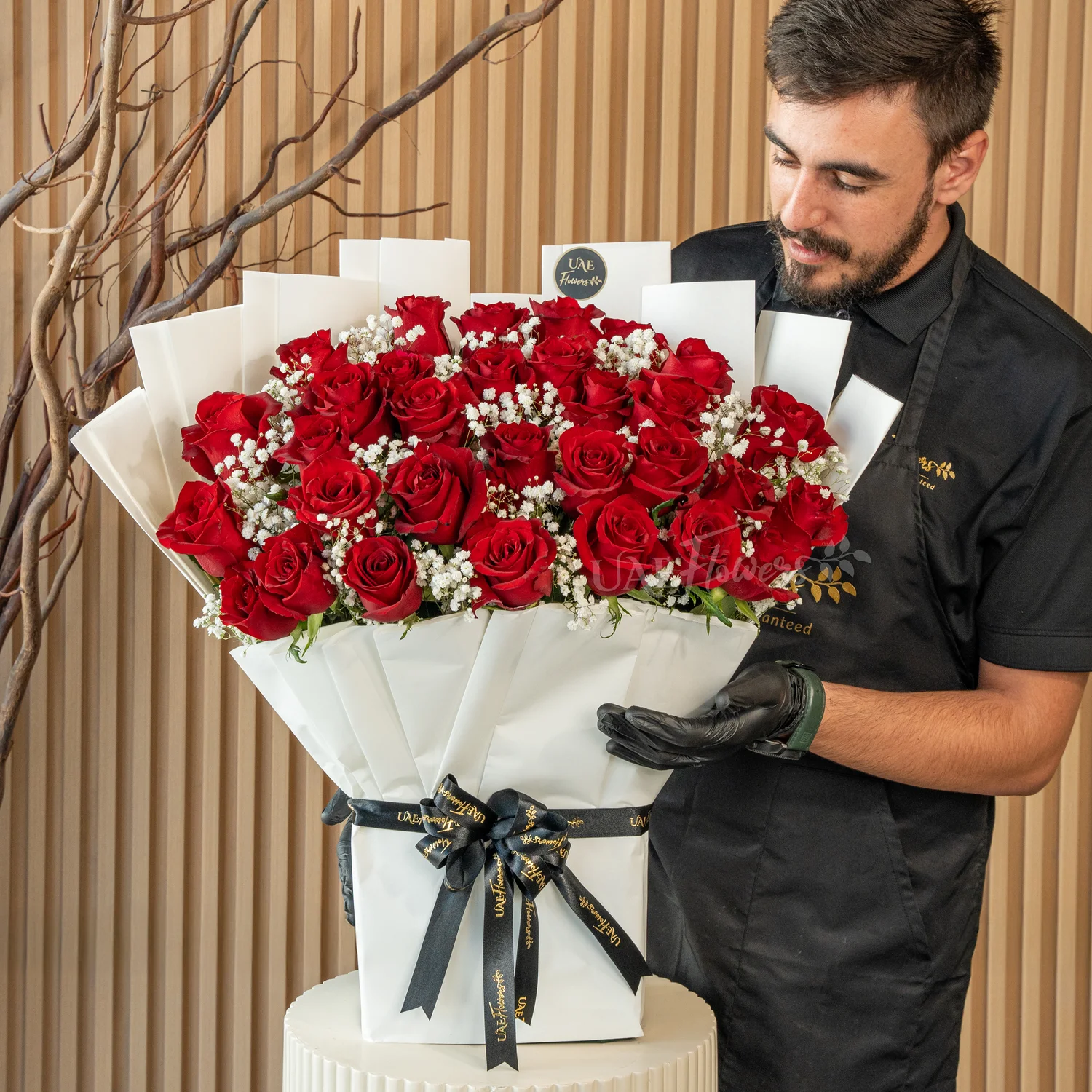 Bouquet of 30 red roses with green fillers in paper packing tied with ribbons.