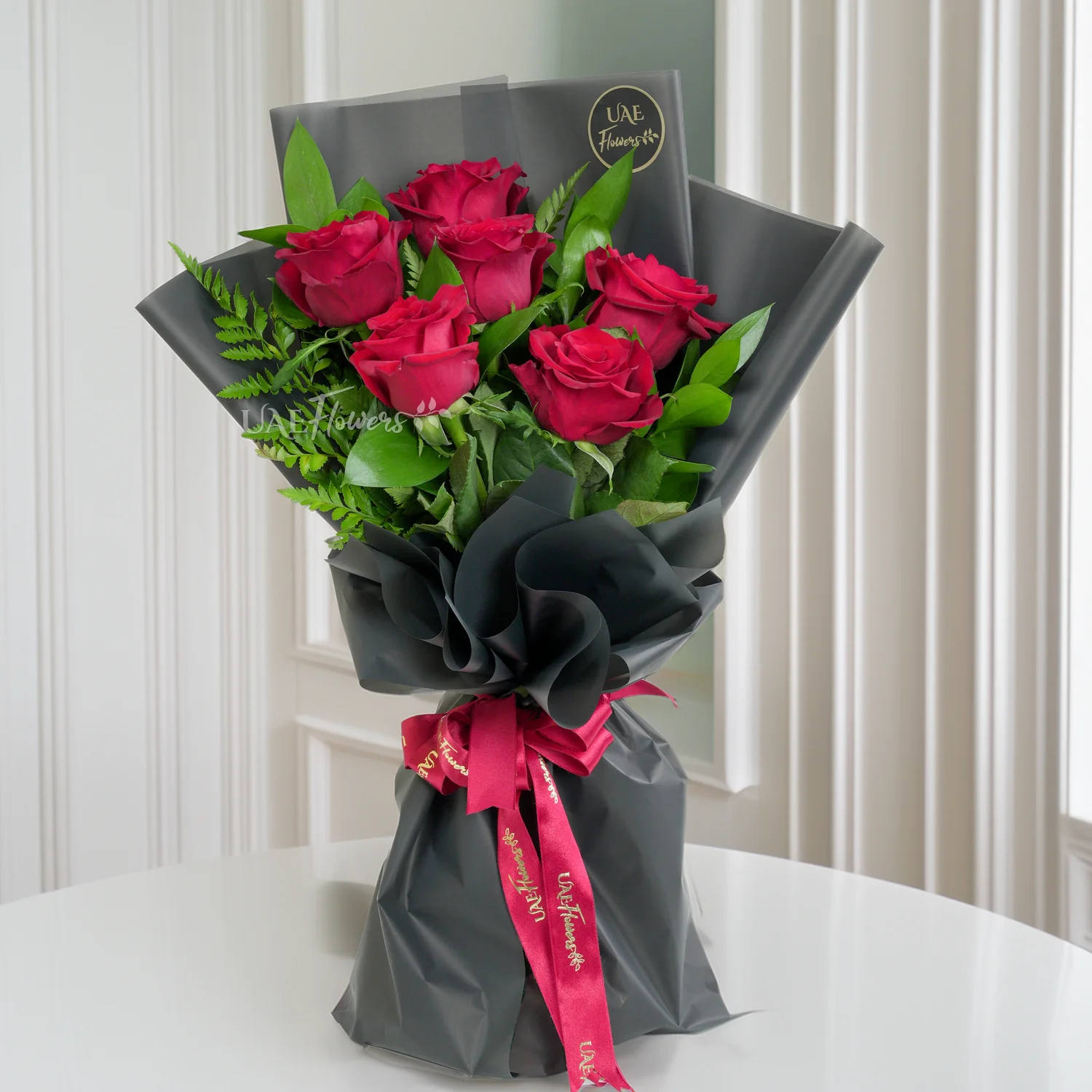 Bouquet of 6 red roses with green fillers in black paper packing tied with ribbons.