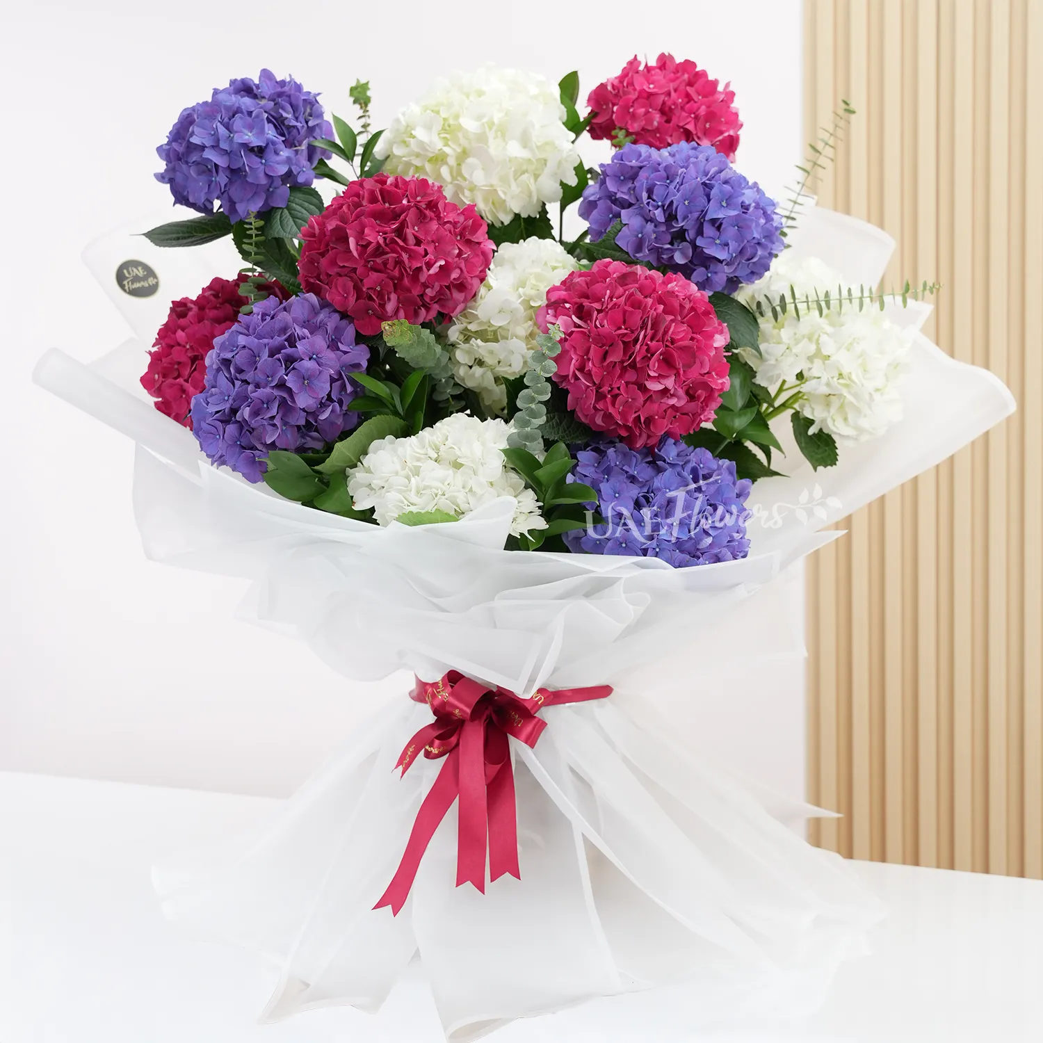 Bouquet of 4 red hydrangeas, 4 white hydrangeas and 4 purple hydrangeas with fillers in white paper packing with ribbons.