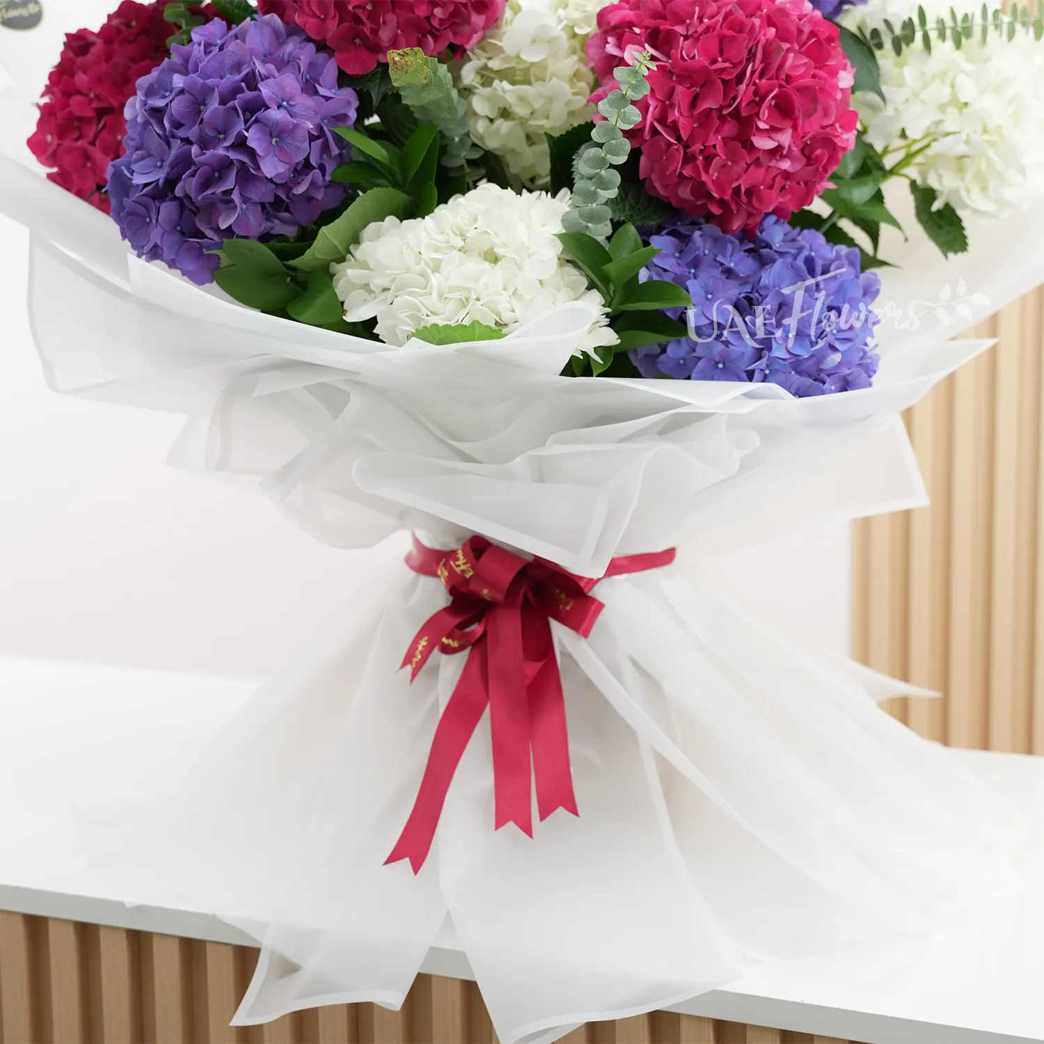Bouquet of 4 red hydrangeas, 4 white hydrangeas and 4 purple hydrangeas with fillers in white paper packing with ribbons.