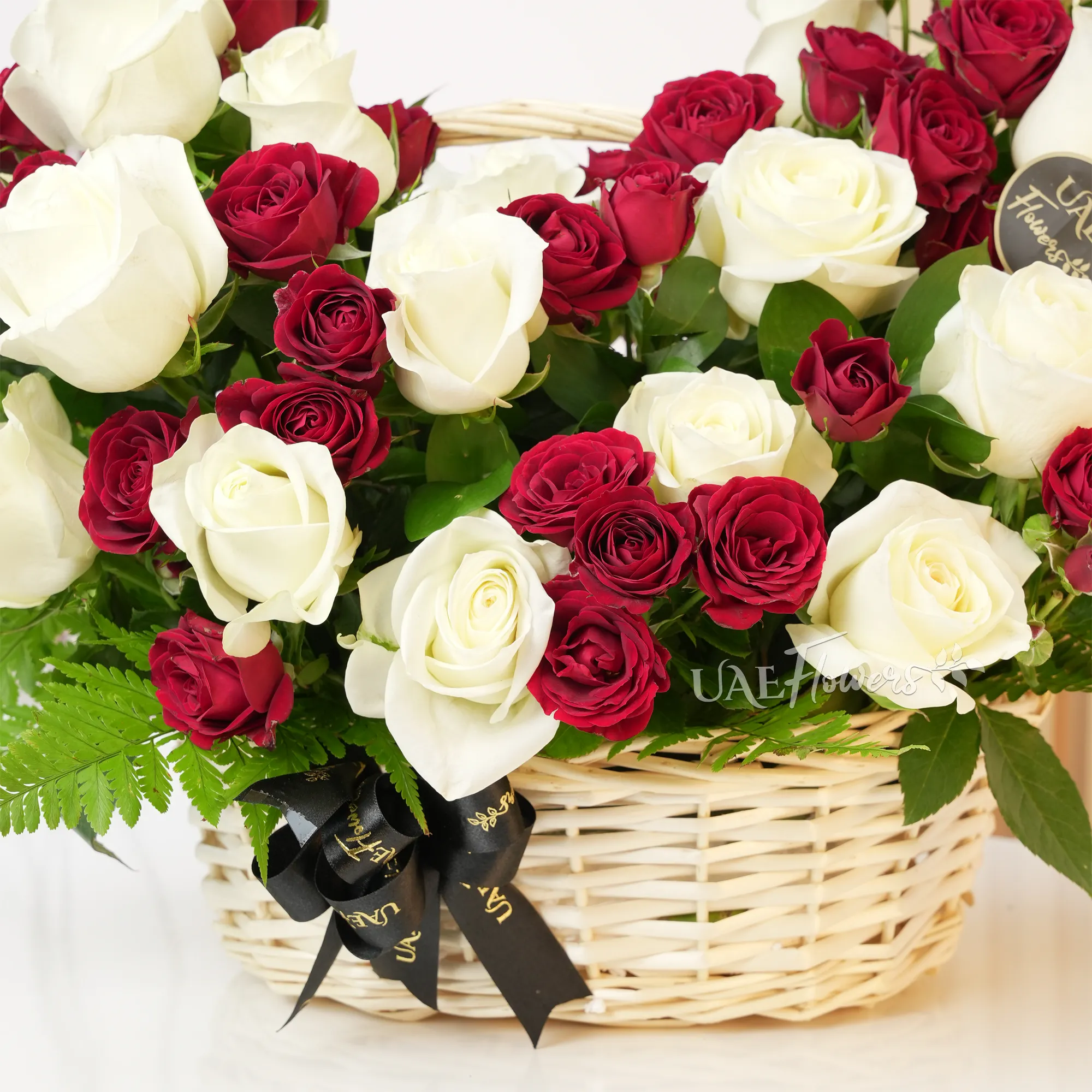 An arrangement of 20 white roses and 5 red spray roses with green fillers in a handle basket.