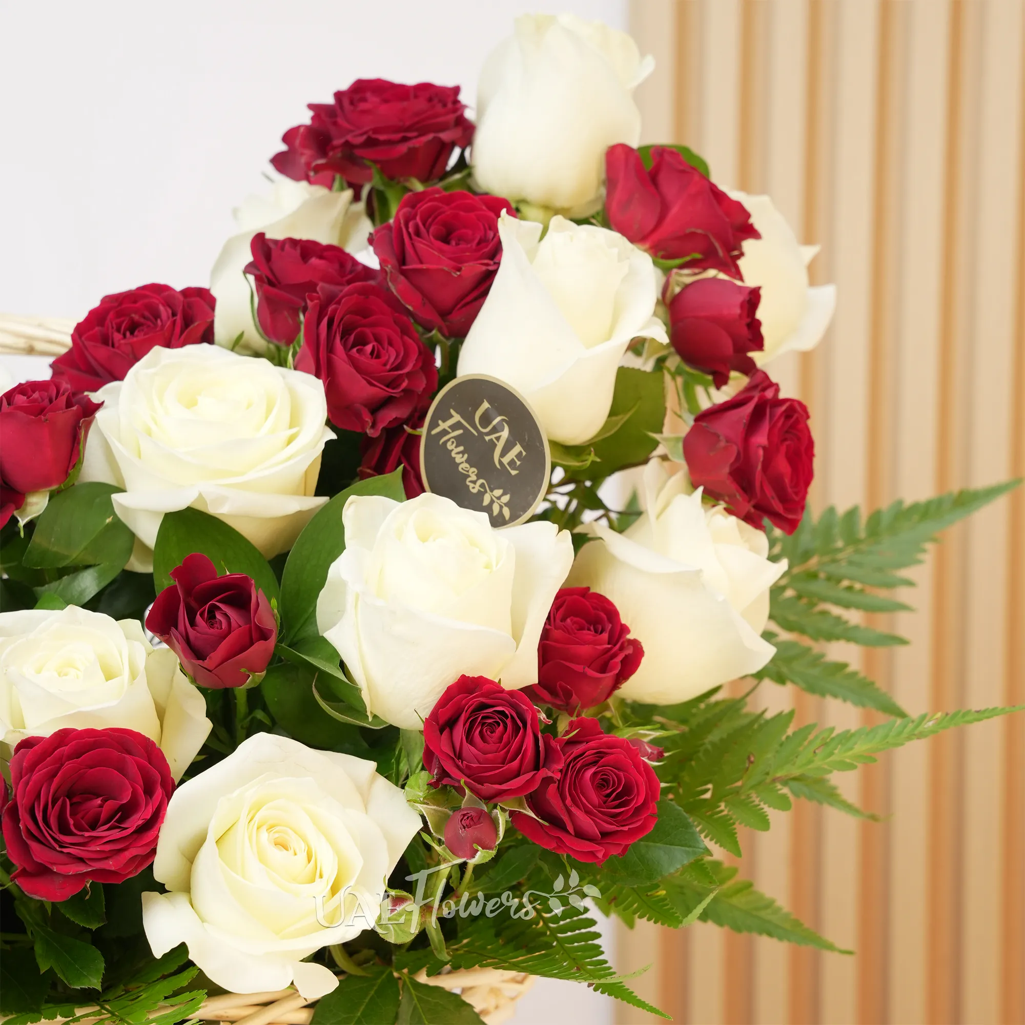 An arrangement of 20 white roses and 5 red spray roses with green fillers in a handle basket.