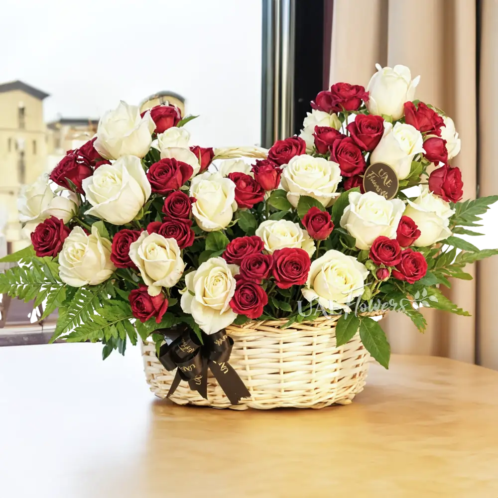An arrangement of 20 white roses and 5 red spray roses with green fillers in a handle basket.
