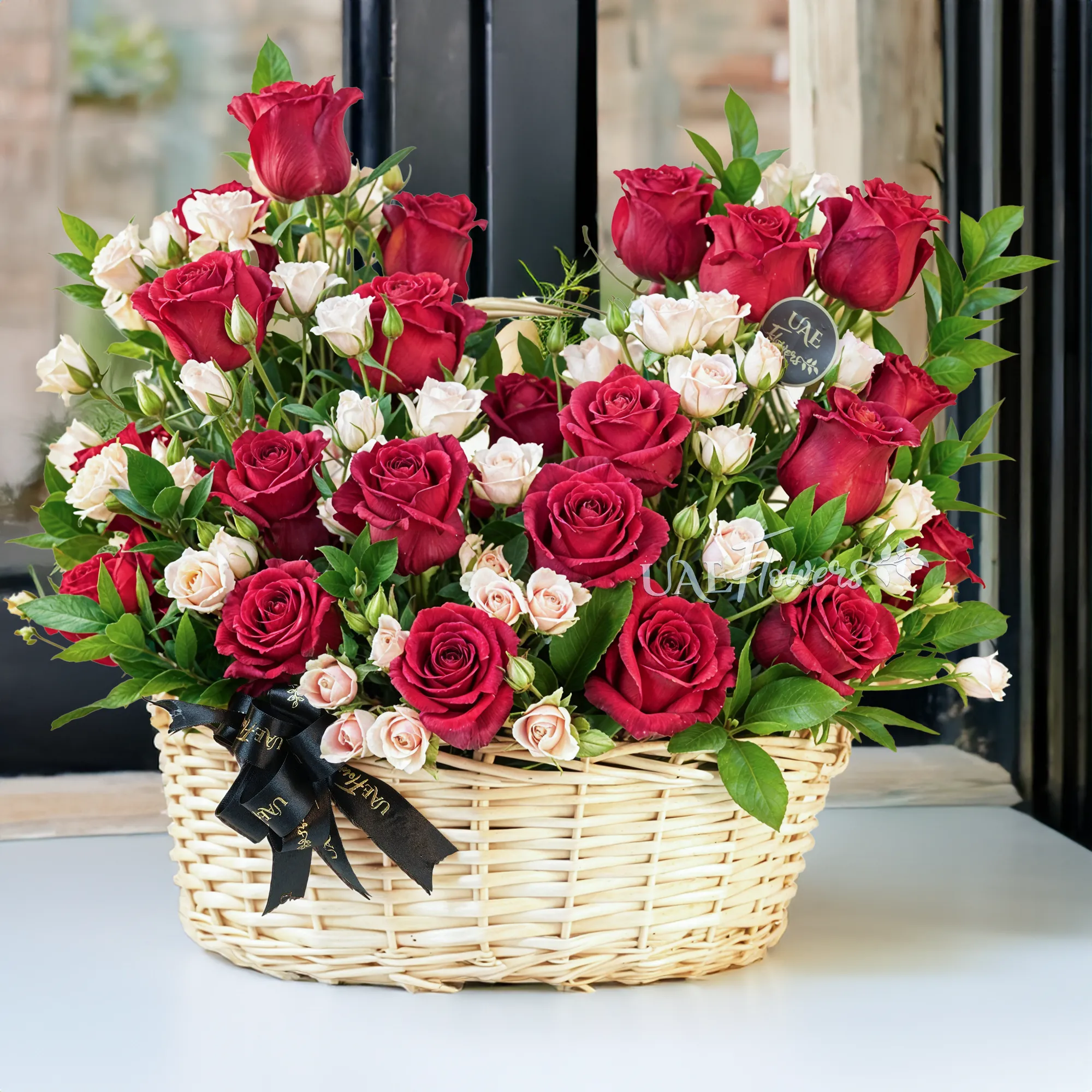 An arrangement of 20 red roses and 6 pink spray roses with green fillers in a handle basket.