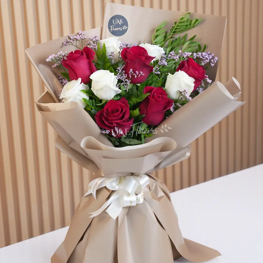 Bouquet of 10 red and white roses with green fillers in wrapping paper and tied with ribbons.