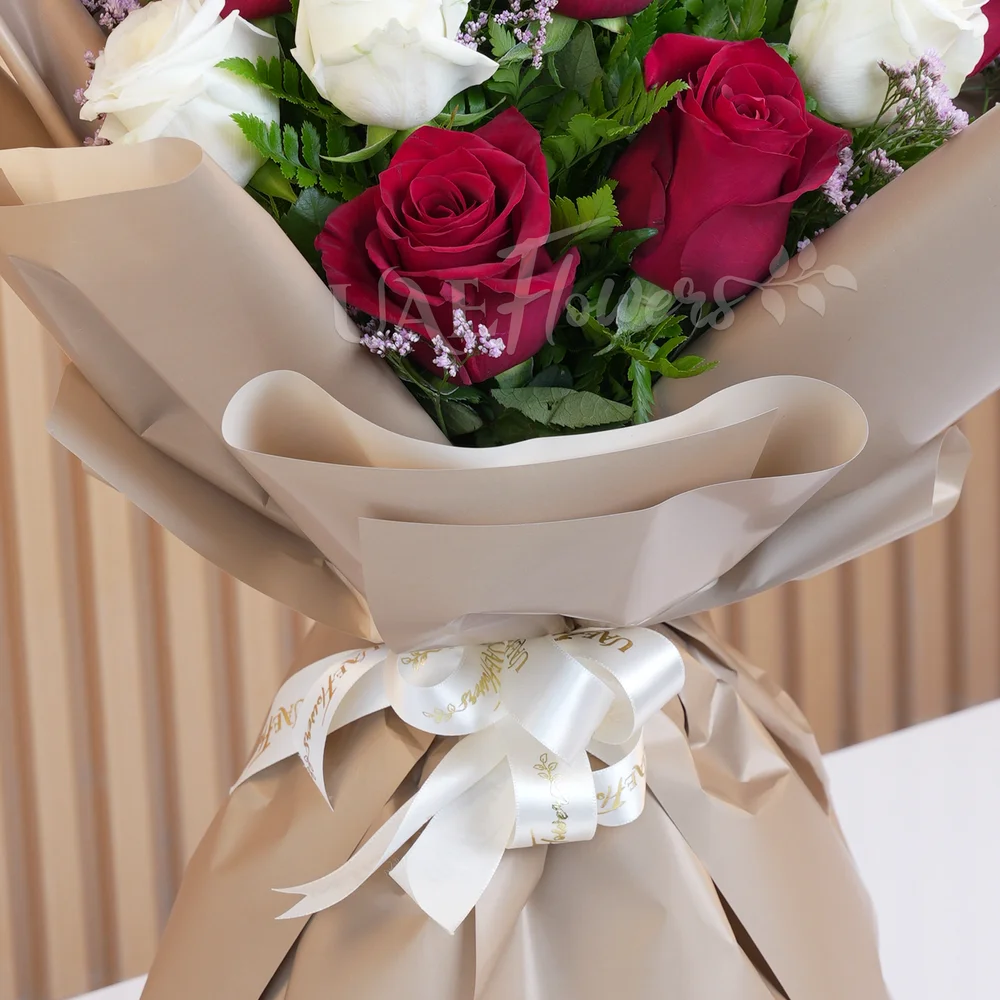 Bouquet of 10 red and white roses with green fillers in wrapping paper and tied with ribbons.