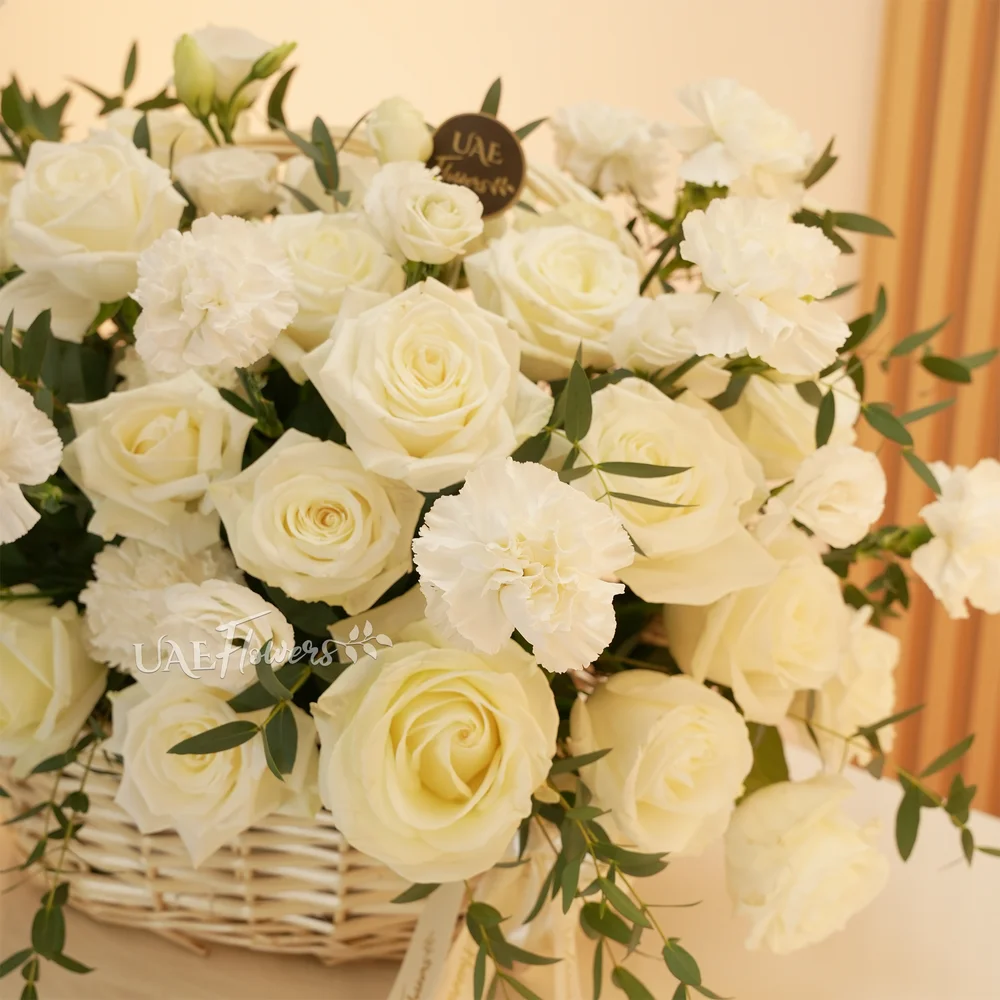 A basket arrangement of 15 white carnations and 15 white roses and fillers.