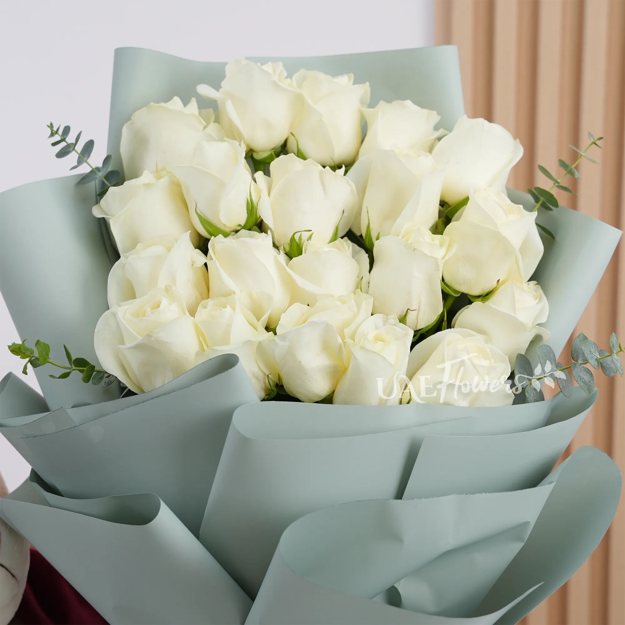 Bouquet of 20 white roses with green fillers in paper packing tied with white ribbons