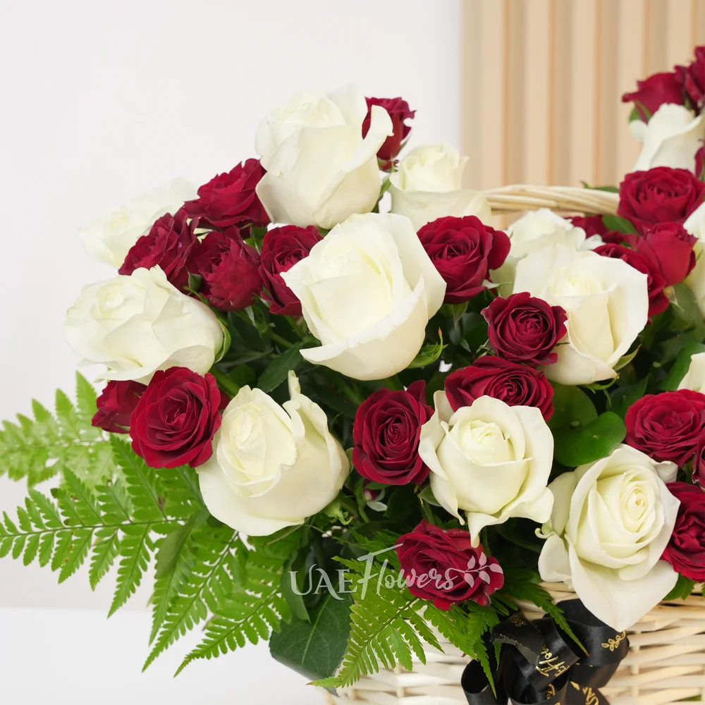 An arrangement of 20 white roses and 5 red spray roses with green fillers in a handle basket.