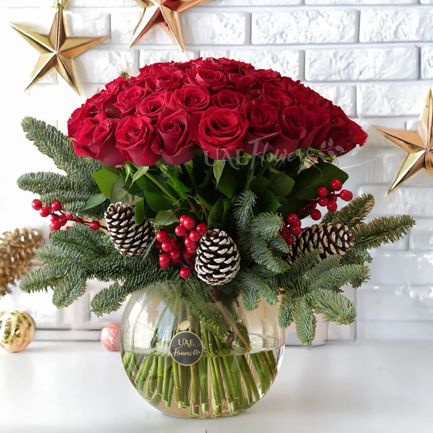 Glass vase arrangement of 50 red roses with pinecones, hypericums and pine leaf.
